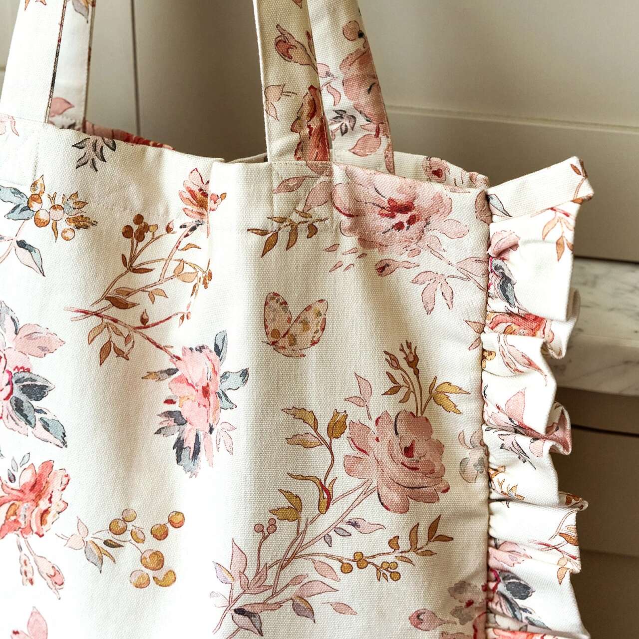 Baumwoll-Tragetasche von Sophie Allport: Nahaufnahme des floralen Musters mit rosa Rosen, Schmetterling und Rüschen am Rand
